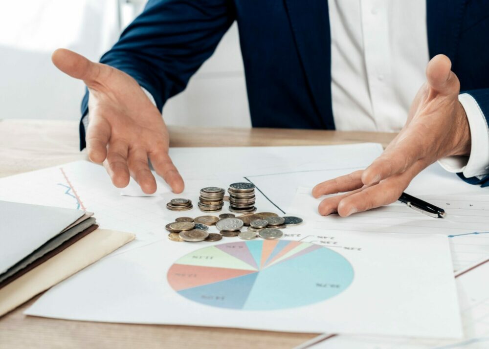 Close-up of a businessperson's hands explaining financial data with coins and charts on the table