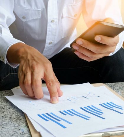 Businessman analyzing financial charts on a mobile phone and tablet, illustrating finance department functions in a company.